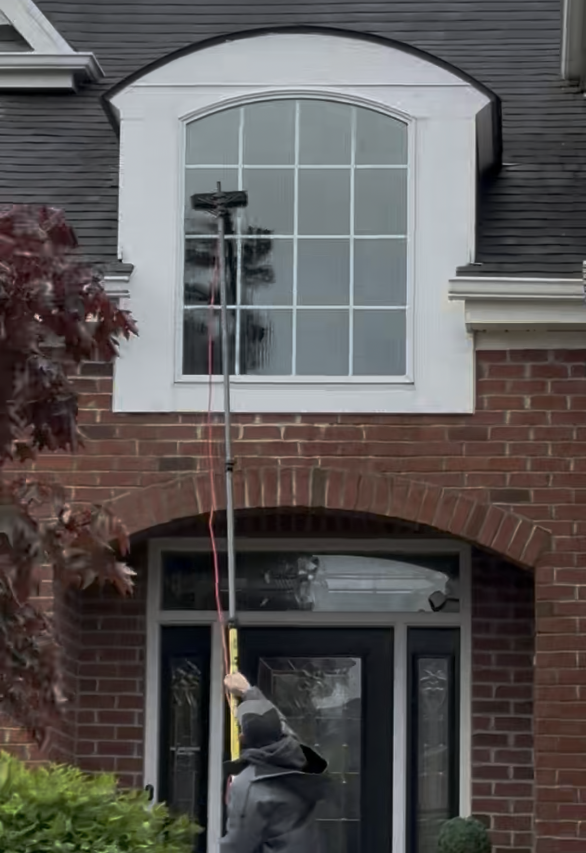 A window cleaner wearing a harness and cap, suspended by ropes, washes a glass facade on a tall building.