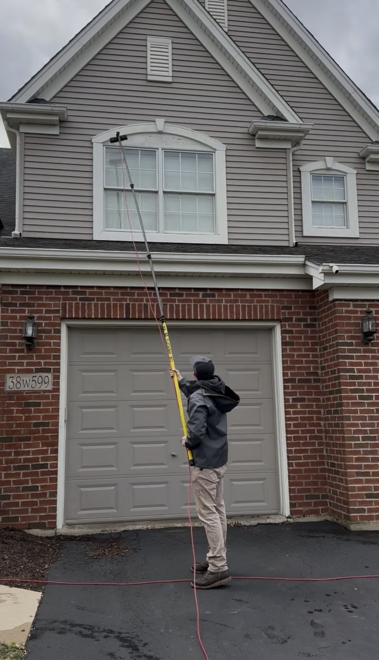 A person pressure washing a residential tile roof against a blue sky.