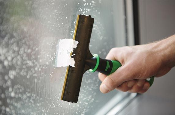 Four professional cleaners in uniform and hard hats clean a bright, modern office space with various tools and supplies.