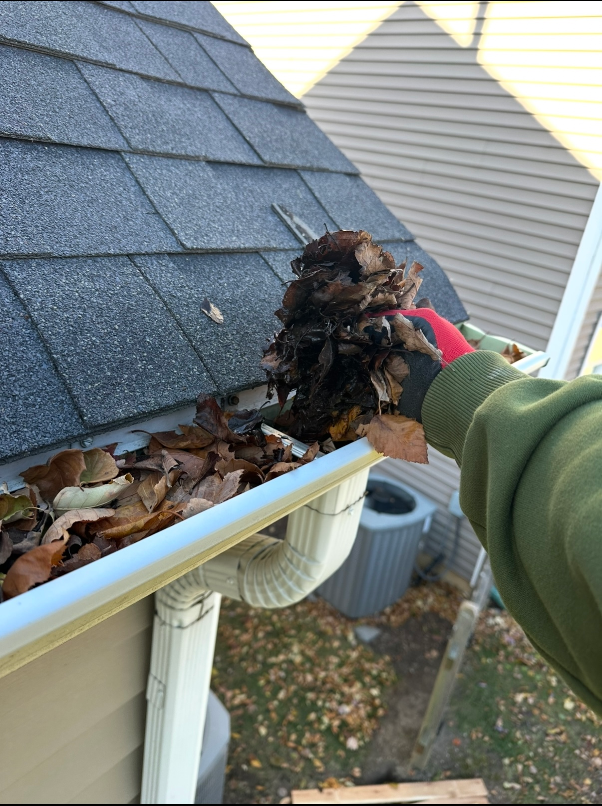 A person uses a pressure washer to clean a dirty residential gutter along a roofline.