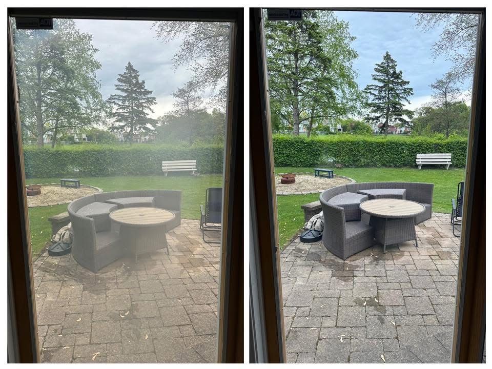 A person in a white protective suit cleans a large window with a squeegee, with a bucket and step ladder nearby.