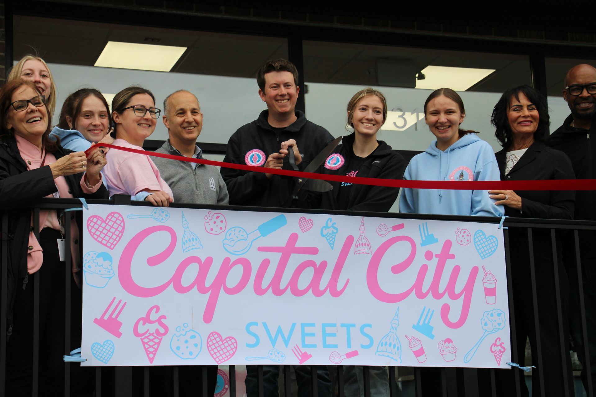 A group of people are standing in front of a sign that says capital city sweets