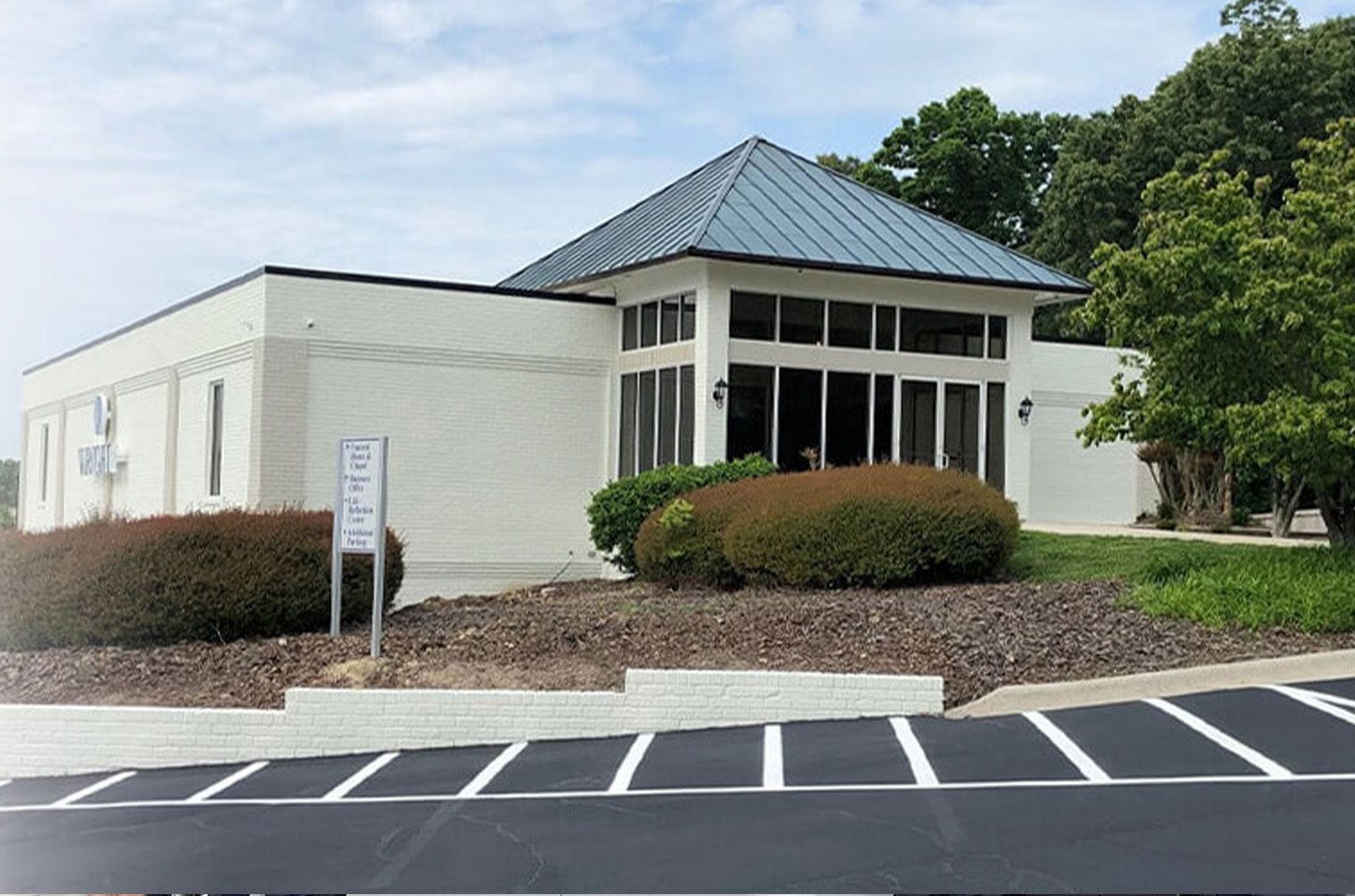 A white building with a blue roof and a parking lot in front of it.