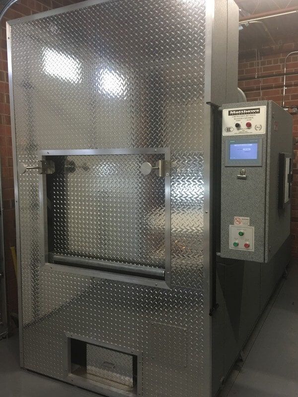 A large stainless steel machine is sitting in a room next to a brick wall.