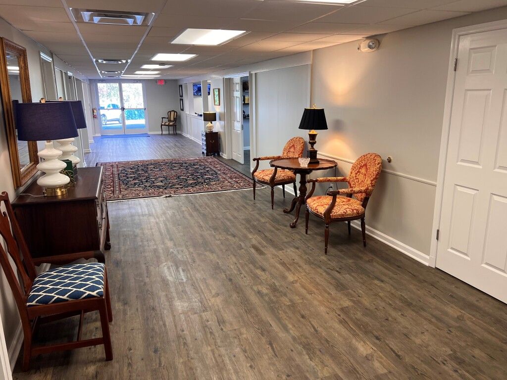 A long hallway with wooden floors , chairs , tables and lamps.