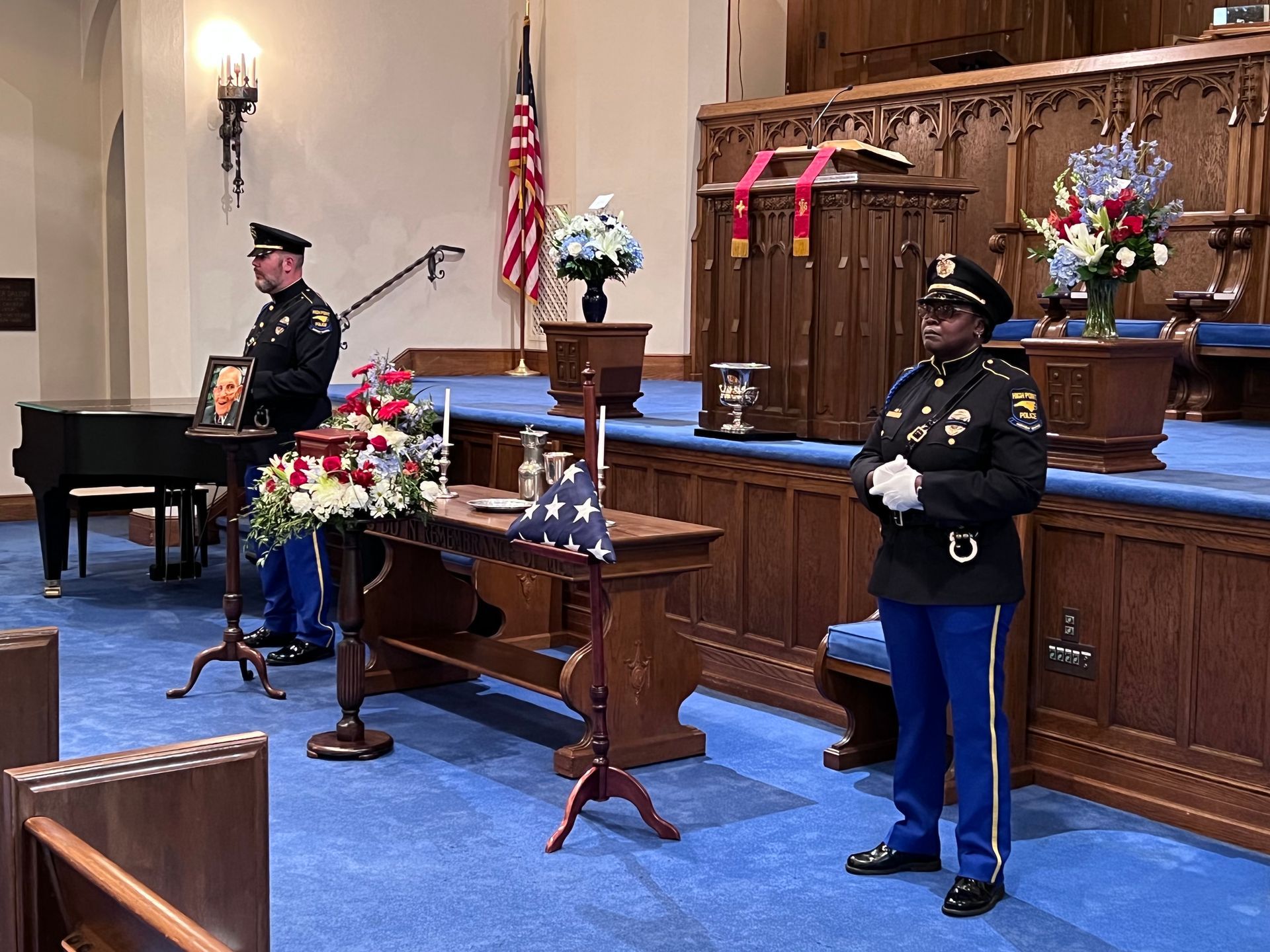 A row of empty chairs in a room with a table and flowers on it.