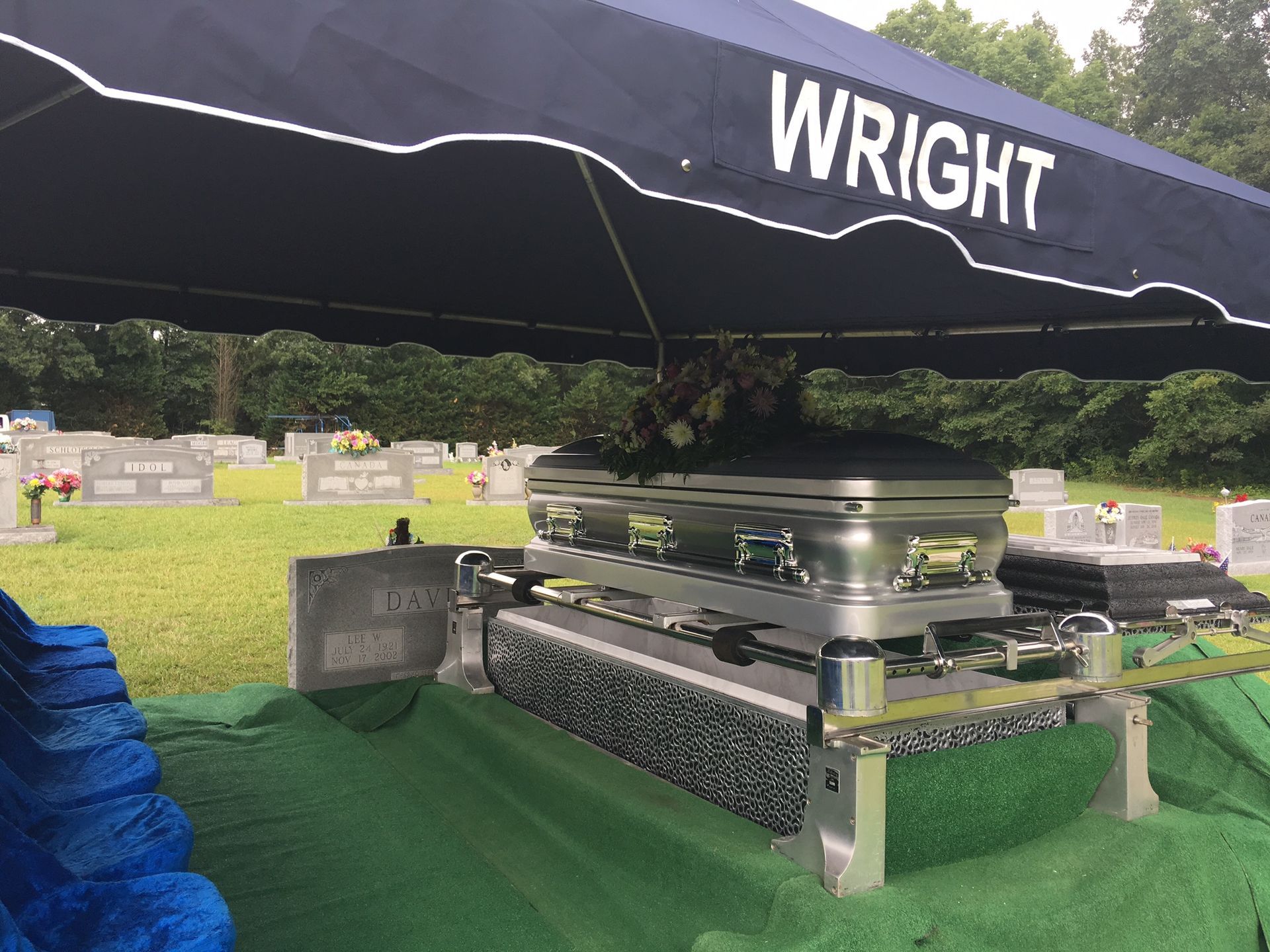 A coffin is under an umbrella with the name wright on it.