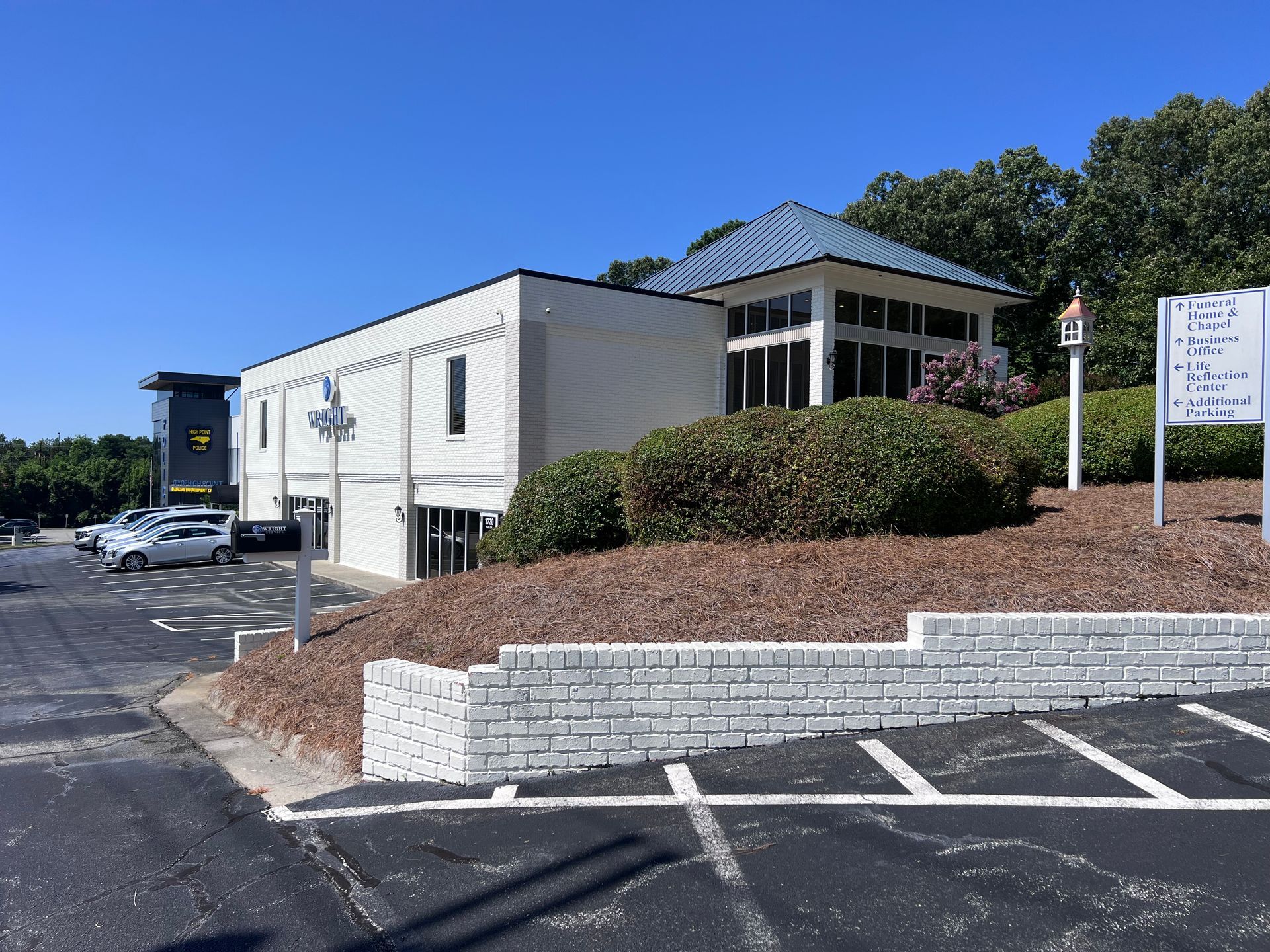 A large white building with a blue roof is sitting next to a parking lot.
