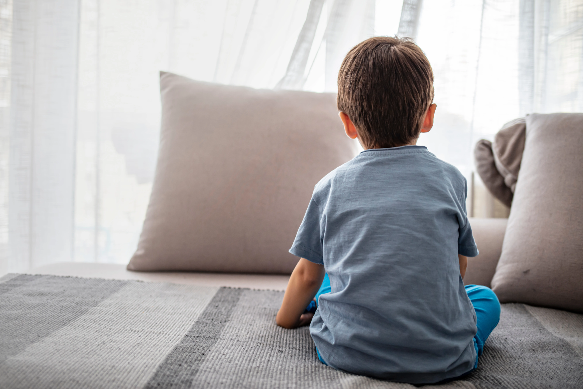 A young boy is sitting on a couch looking out a window.