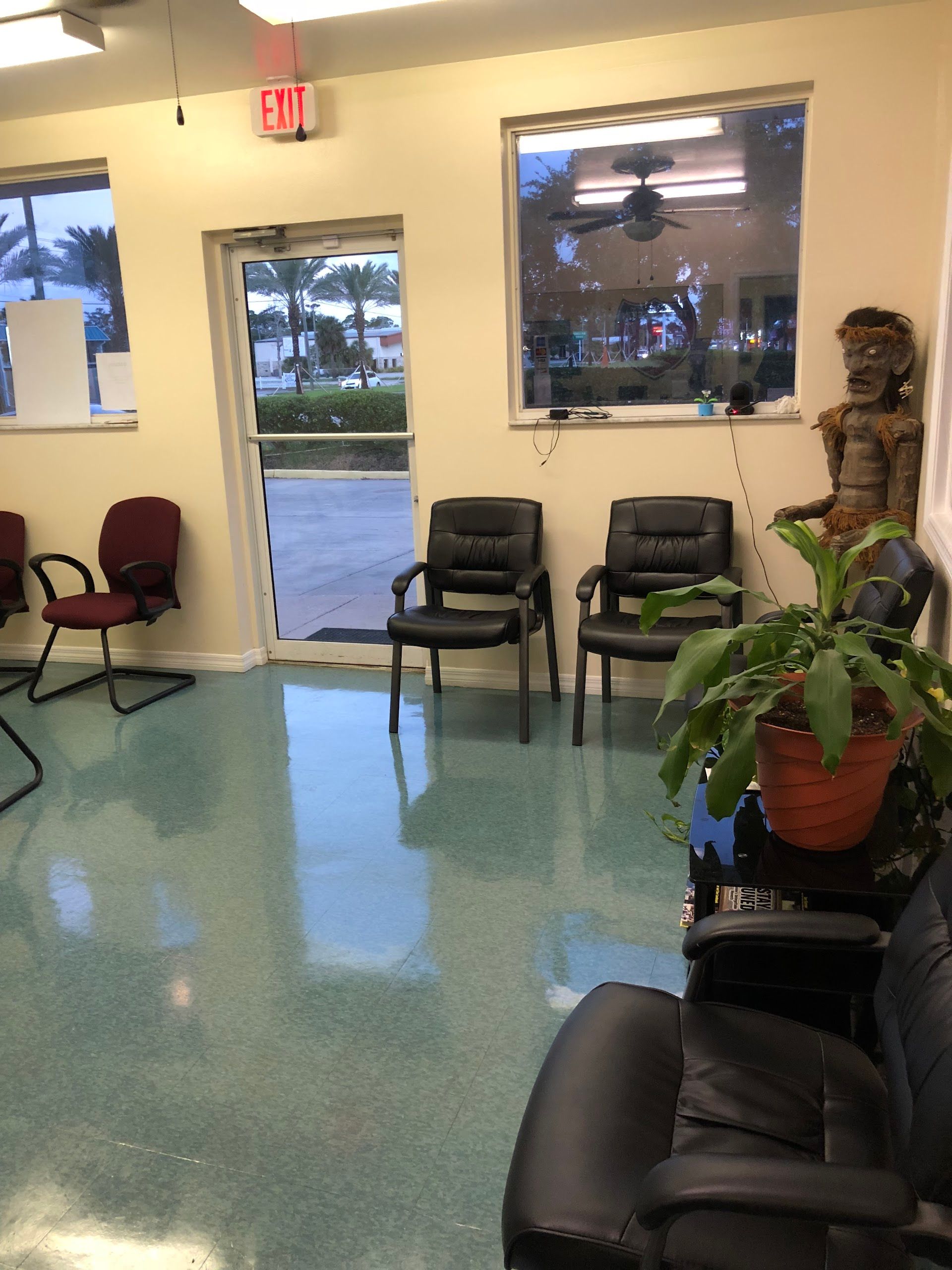 Waiting room with chairs, a plant, and a view through a door. Teal floor, beige walls | Daytona Automotive