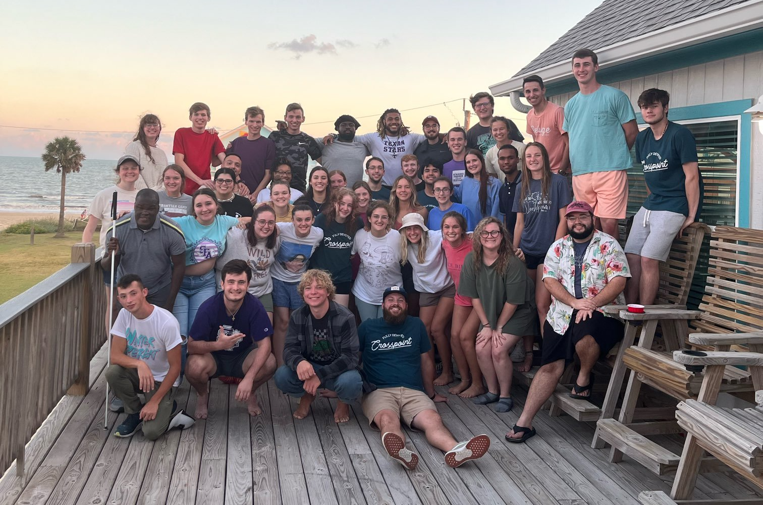 College students posing at Crosspoint Fall Retreat on a wooden deck near the beach at sunset.