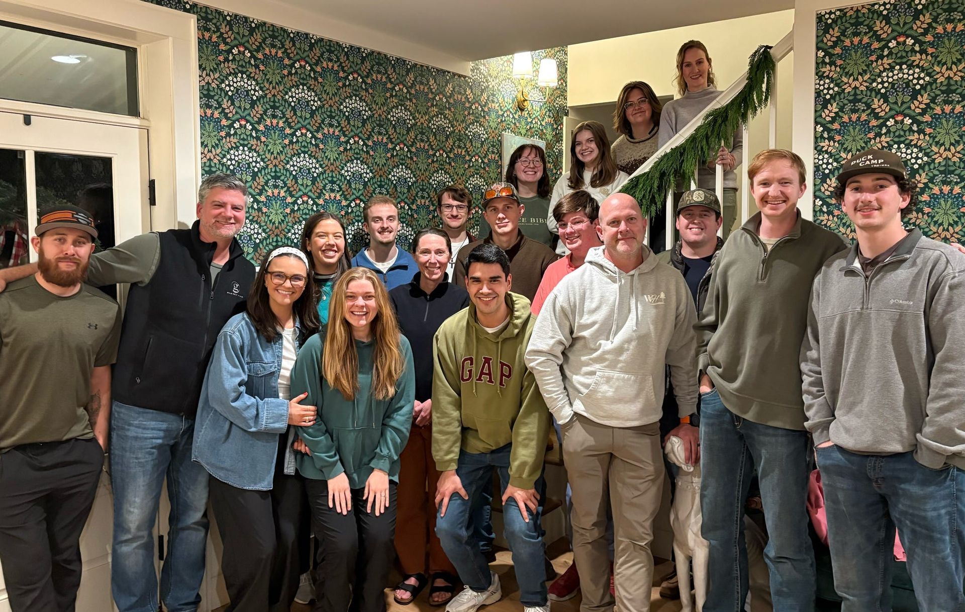 Group of people posing for a photo on a staircase with a green garland.