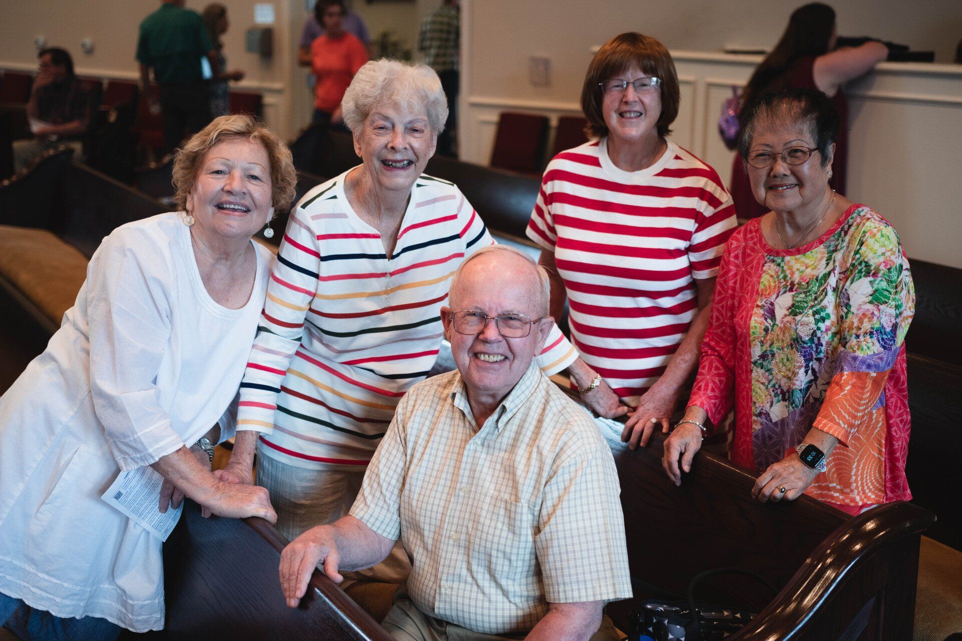 Group of six people smiling near church pews; indoors.