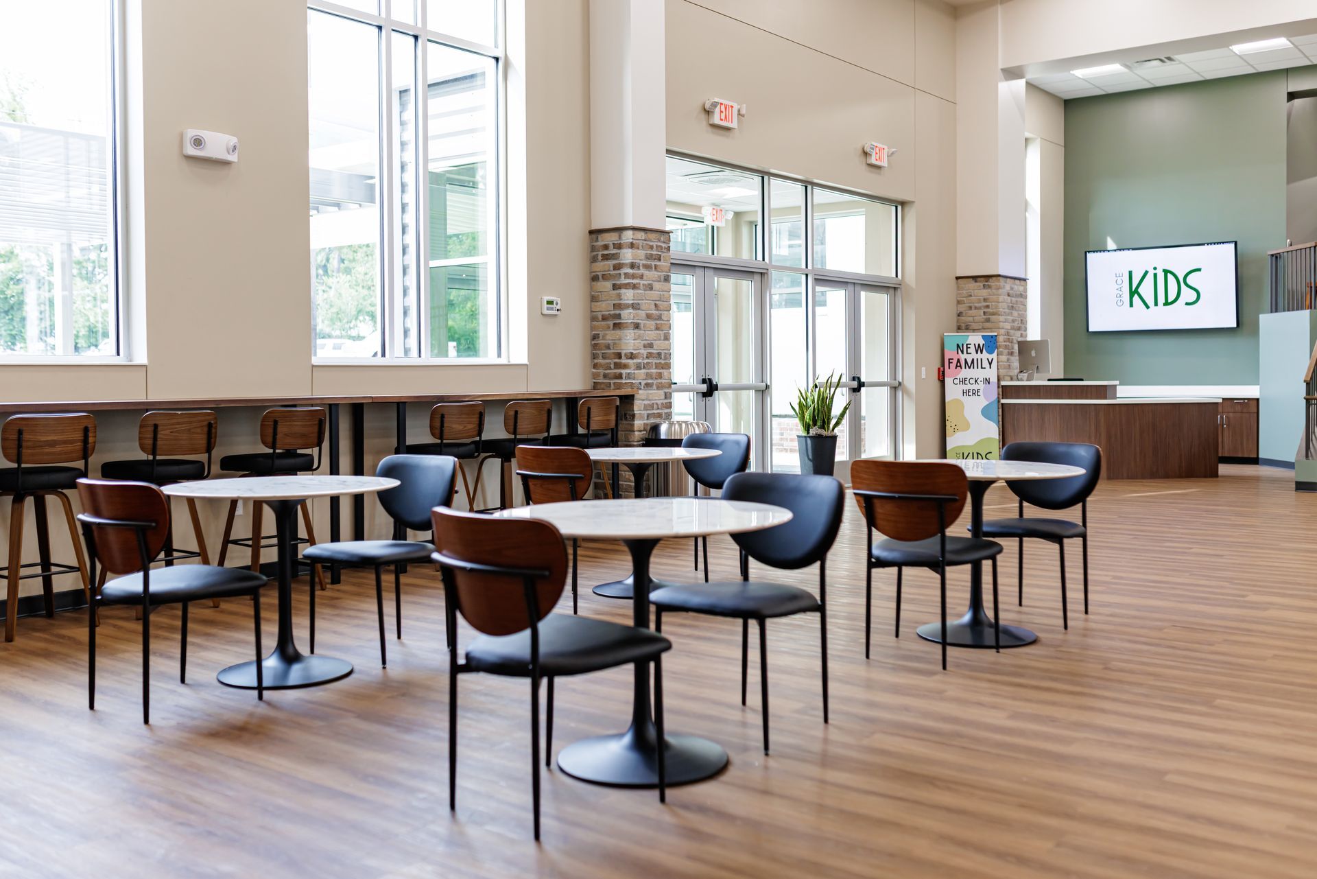 Modern café-style seating area with tables and chairs in a lobby, featuring large windows and a 