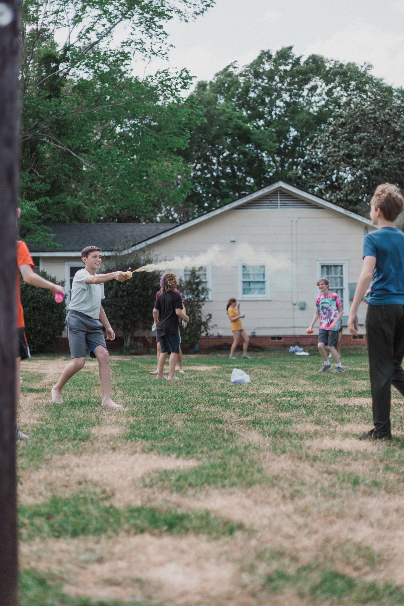 People playing outdoors, a person sprays a cloud of white powder, other people stand nearby.