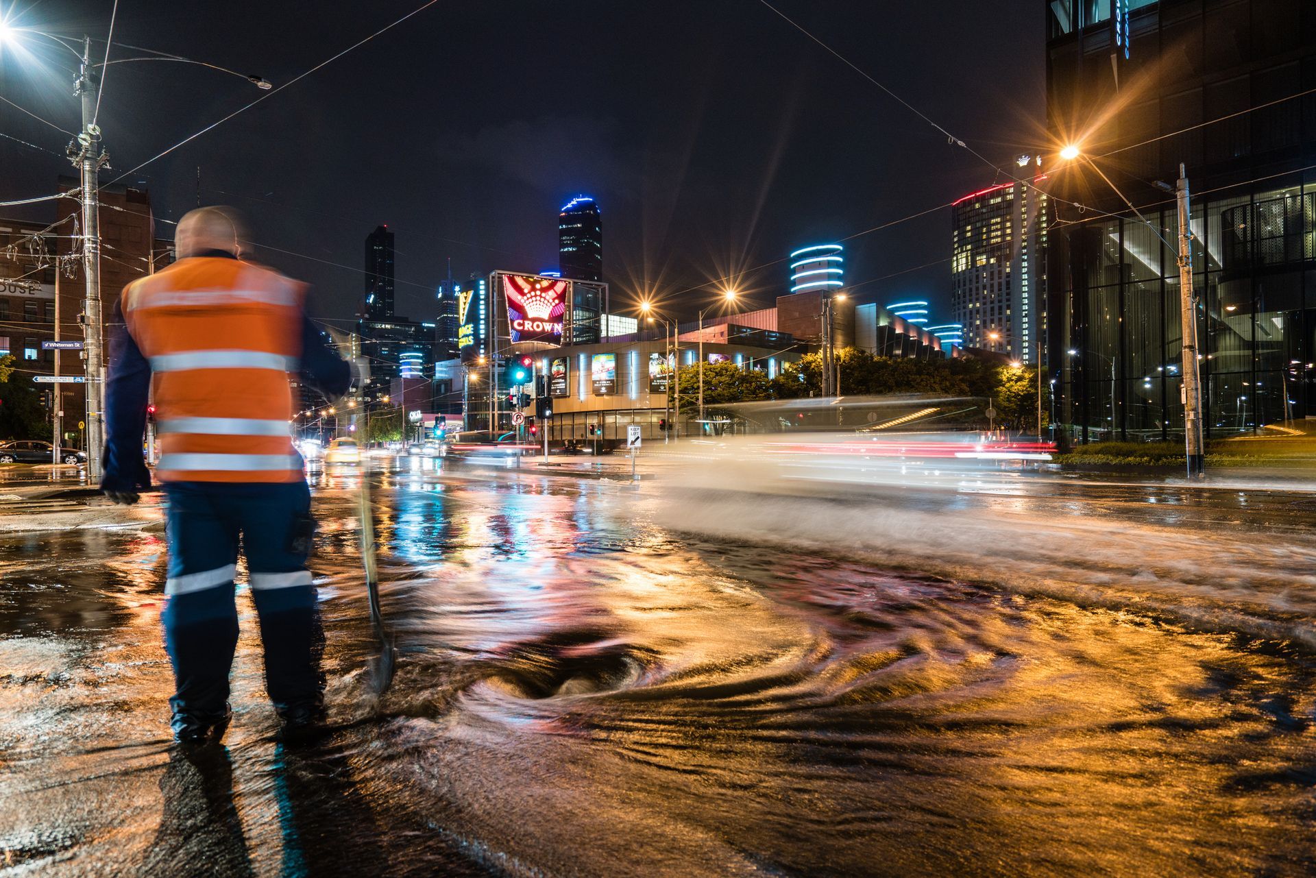 Nighttime storm drain maintenance with worker in safety vest managing urban street flooding.
