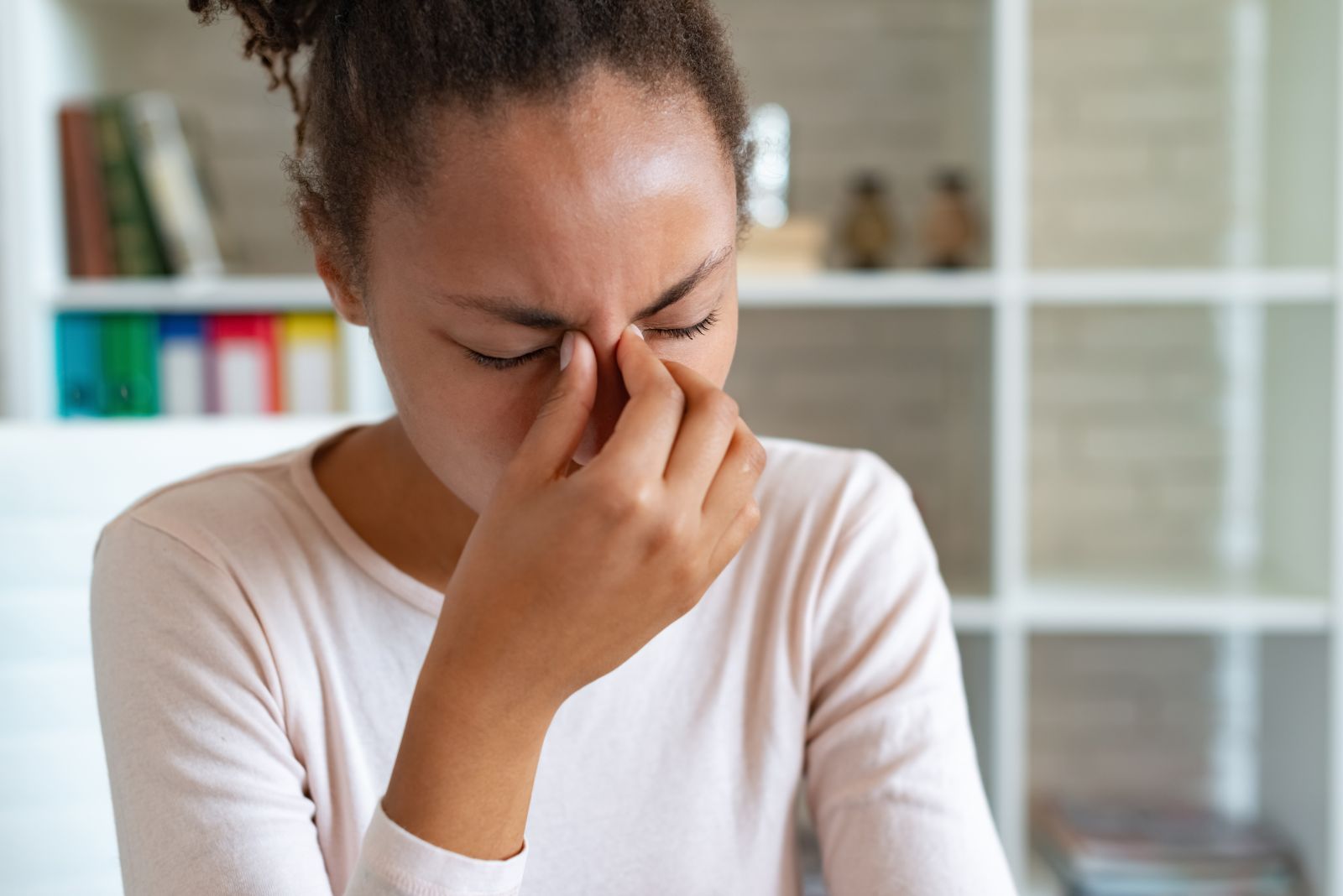 Woman with closed eyes, pressing fingers to her nose and brow, due to sinus pressure