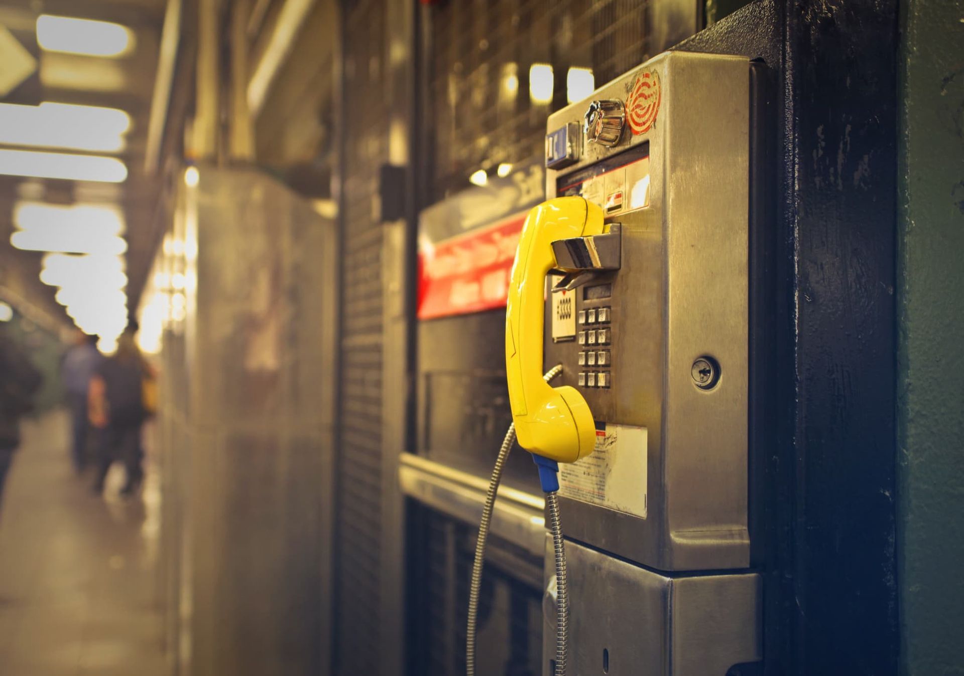 Telefone público amarelo instalado na parede de uma estação de metrô.