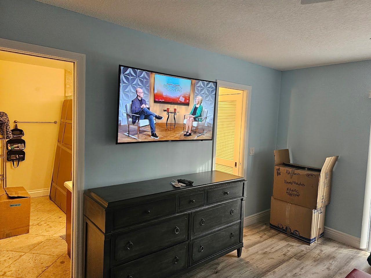 A living room with a dresser and a flat screen tv on the wall.