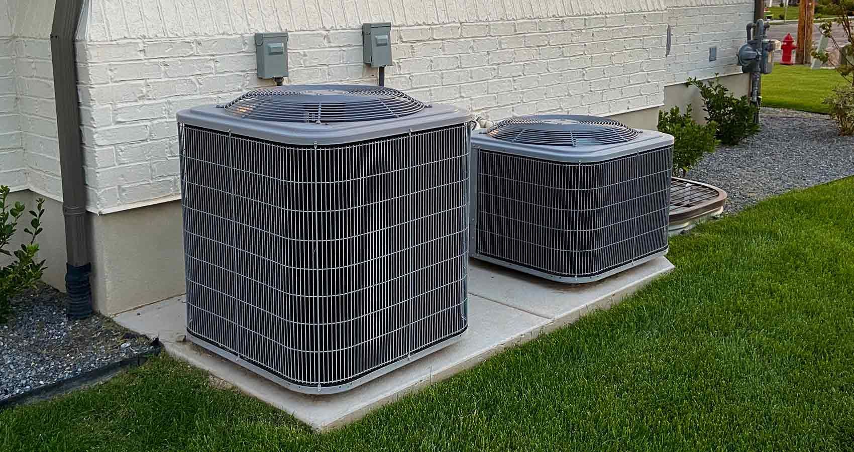 Two air conditioners are sitting on the side of a house.