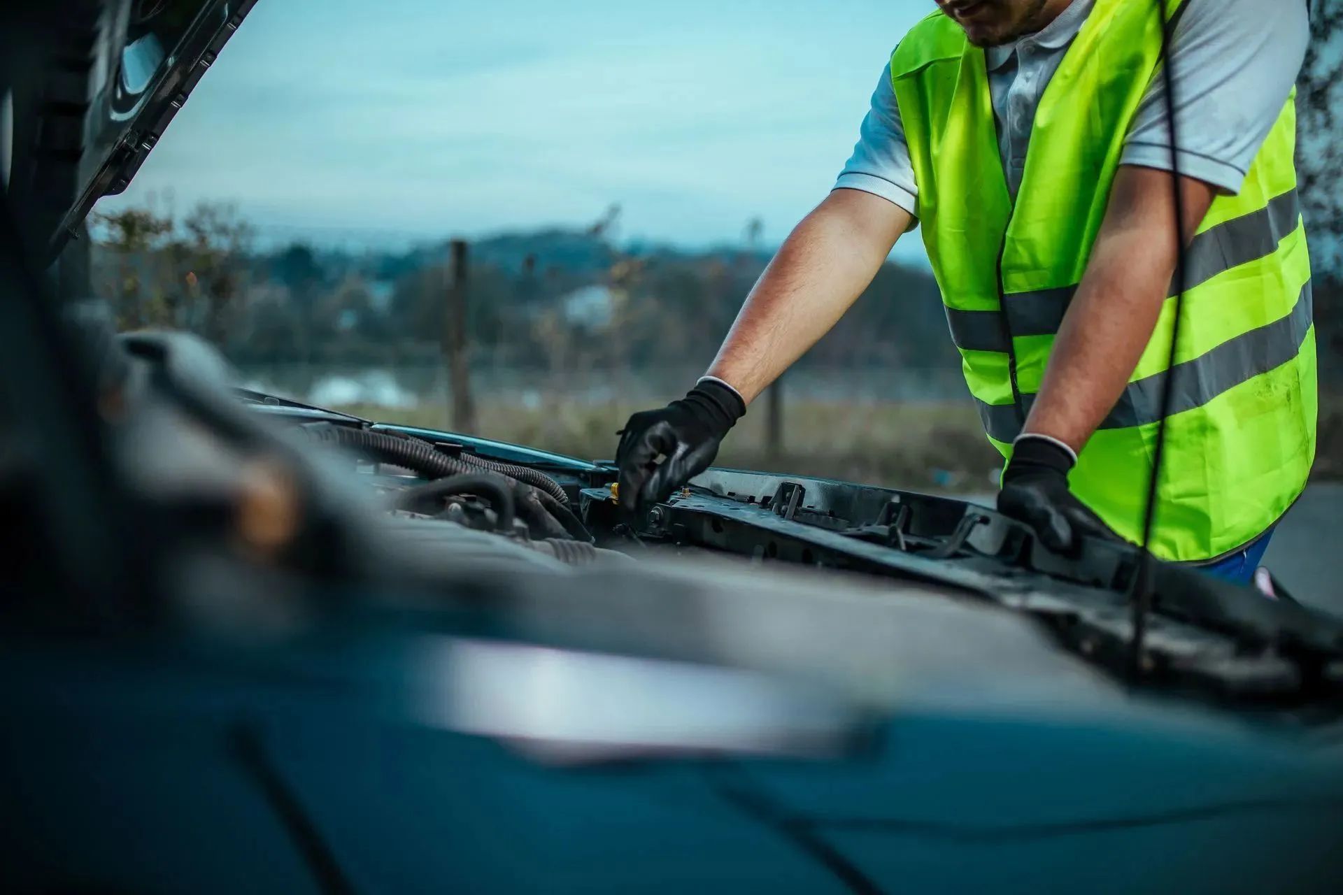 Mechanic wearing a reflective vest looking under the hood of a car