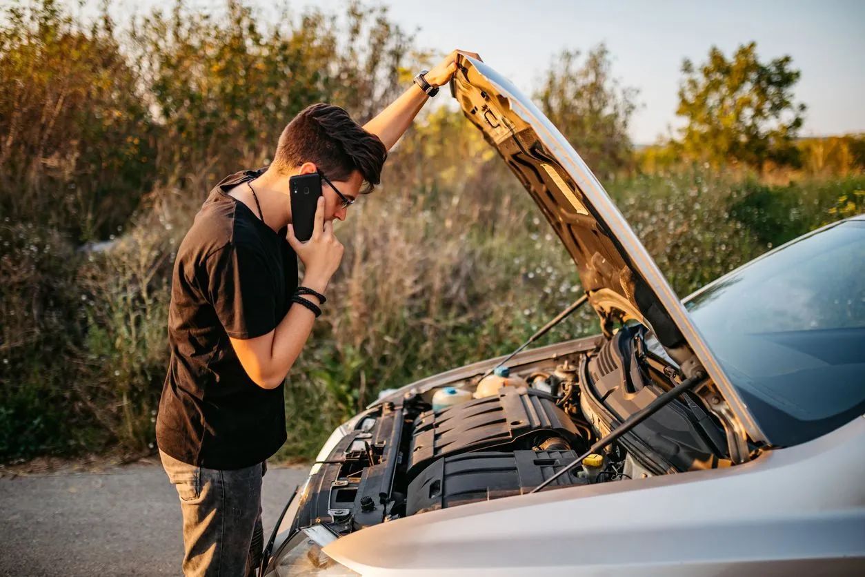Person on the phone standing with car hood open