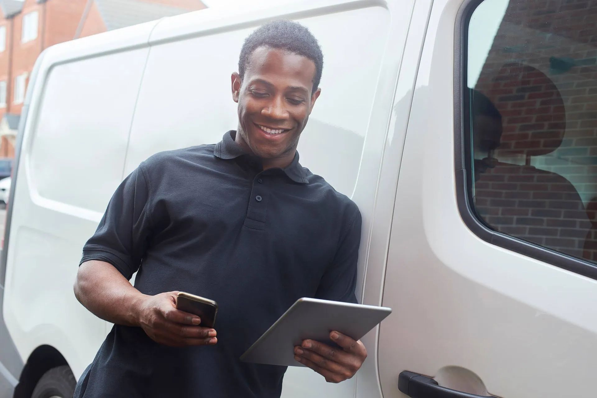 Person standing by a white van holding a phone and tablet