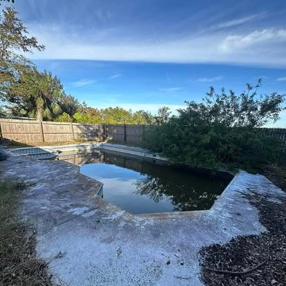An empty swimming pool with a fence and trees in the background.