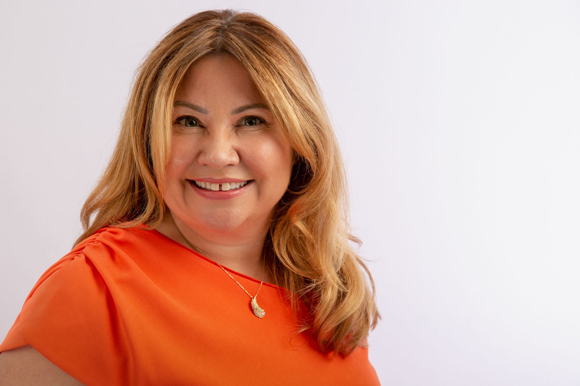 A woman in an orange shirt is smiling and wearing a necklace.