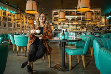 A woman is sitting at a table in a restaurant holding a cup of coffee.