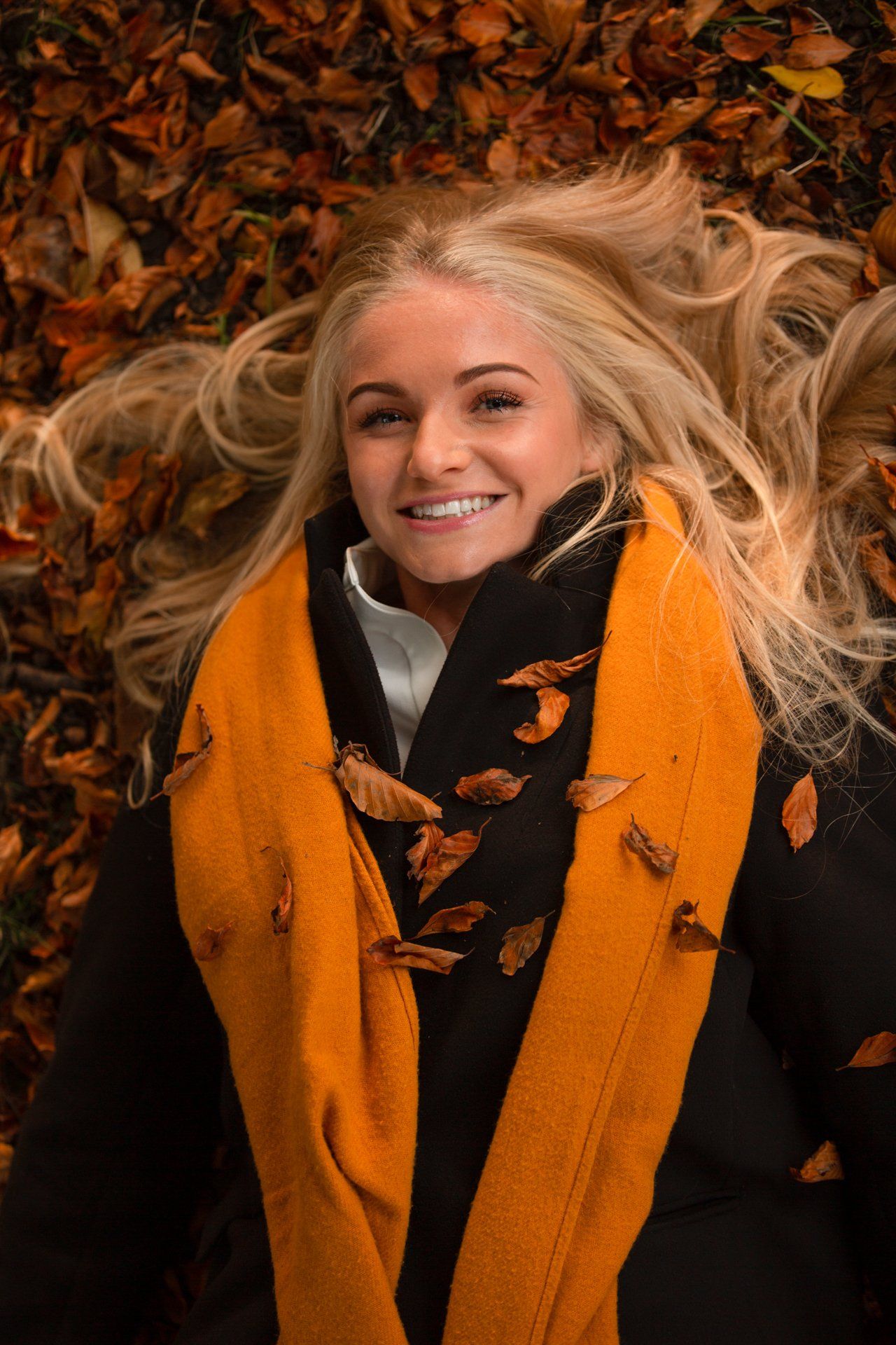 Portrait photography of young woman with orange scarf laying amongst the Autumn leaves