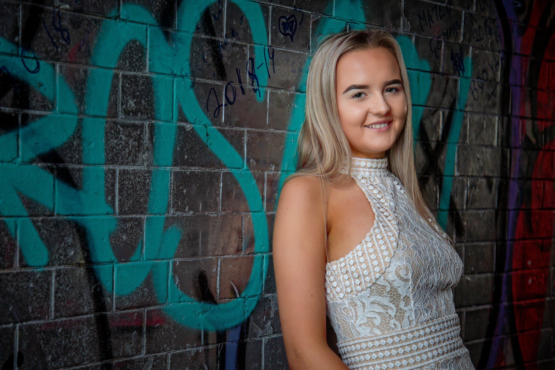 Blond teenager wearing a white lace dress and trainers in graffiti tunnel, Leeds