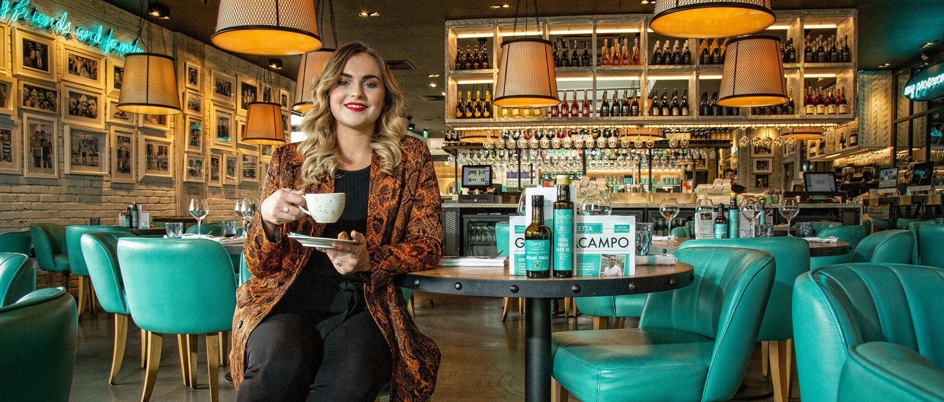 A woman is sitting at a table in a restaurant holding a cup of coffee.