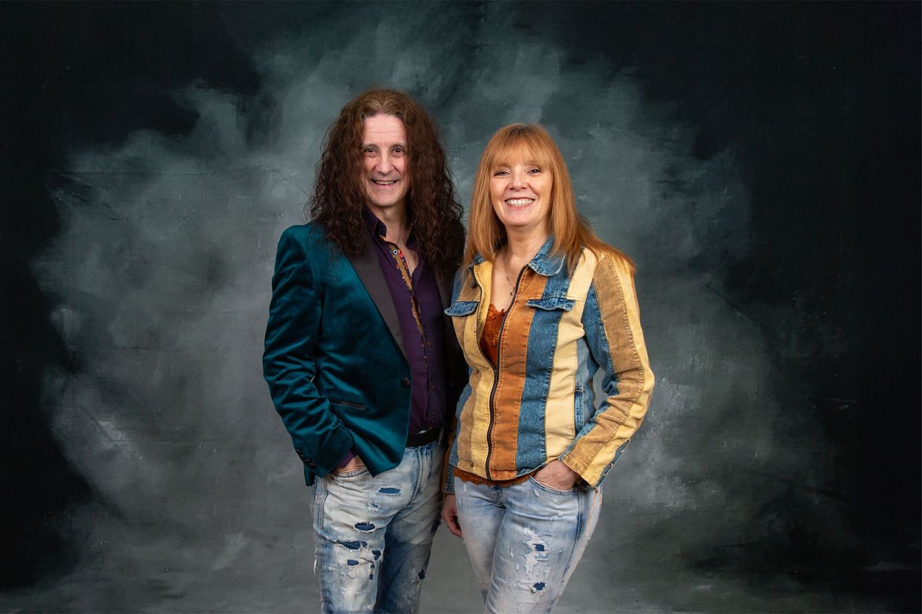 A man and a woman are standing next to each other in front of a smokey background.