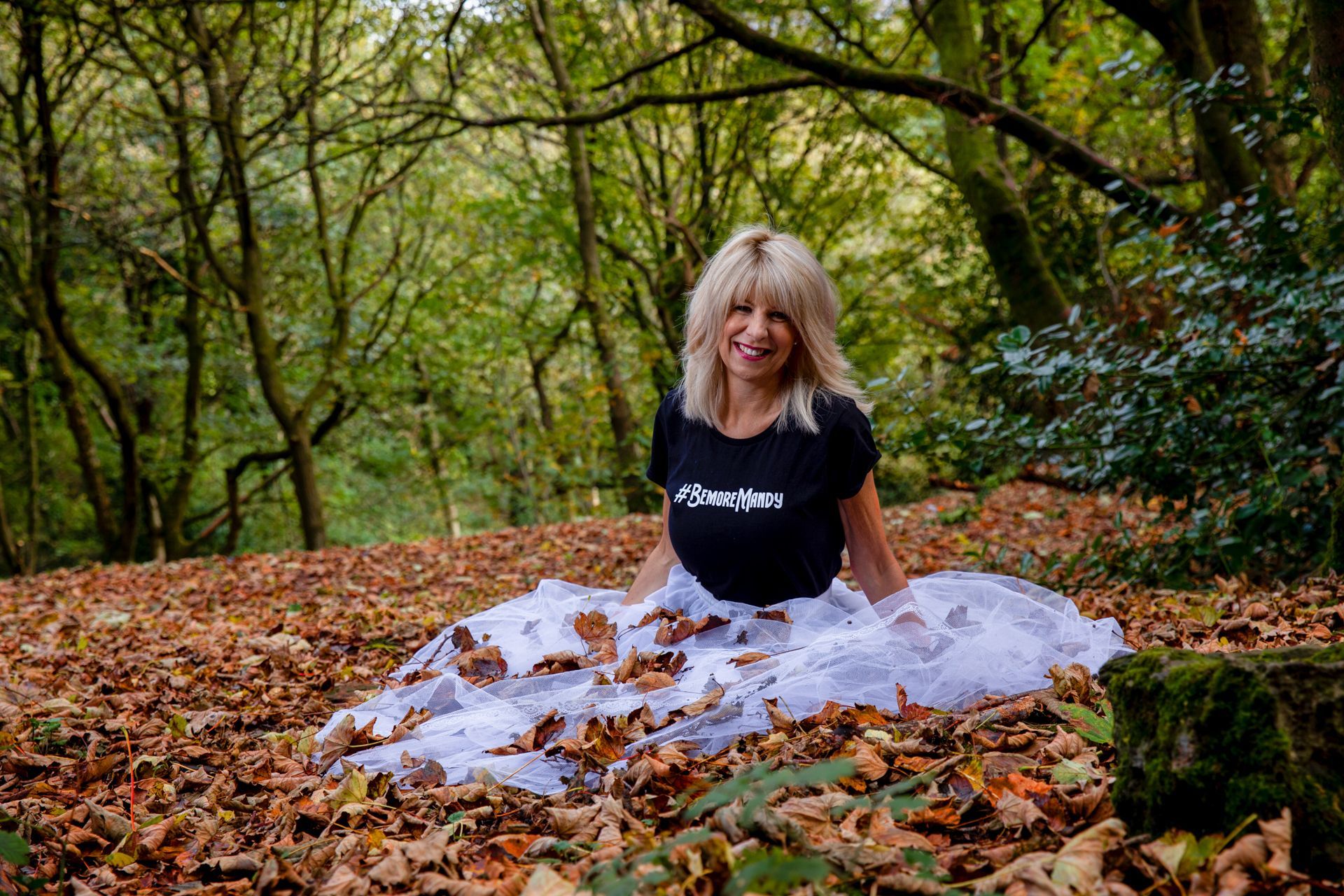 Mandy Taylor MBE wearing #bemoremandy tees-shirt sat in autumn leaves.