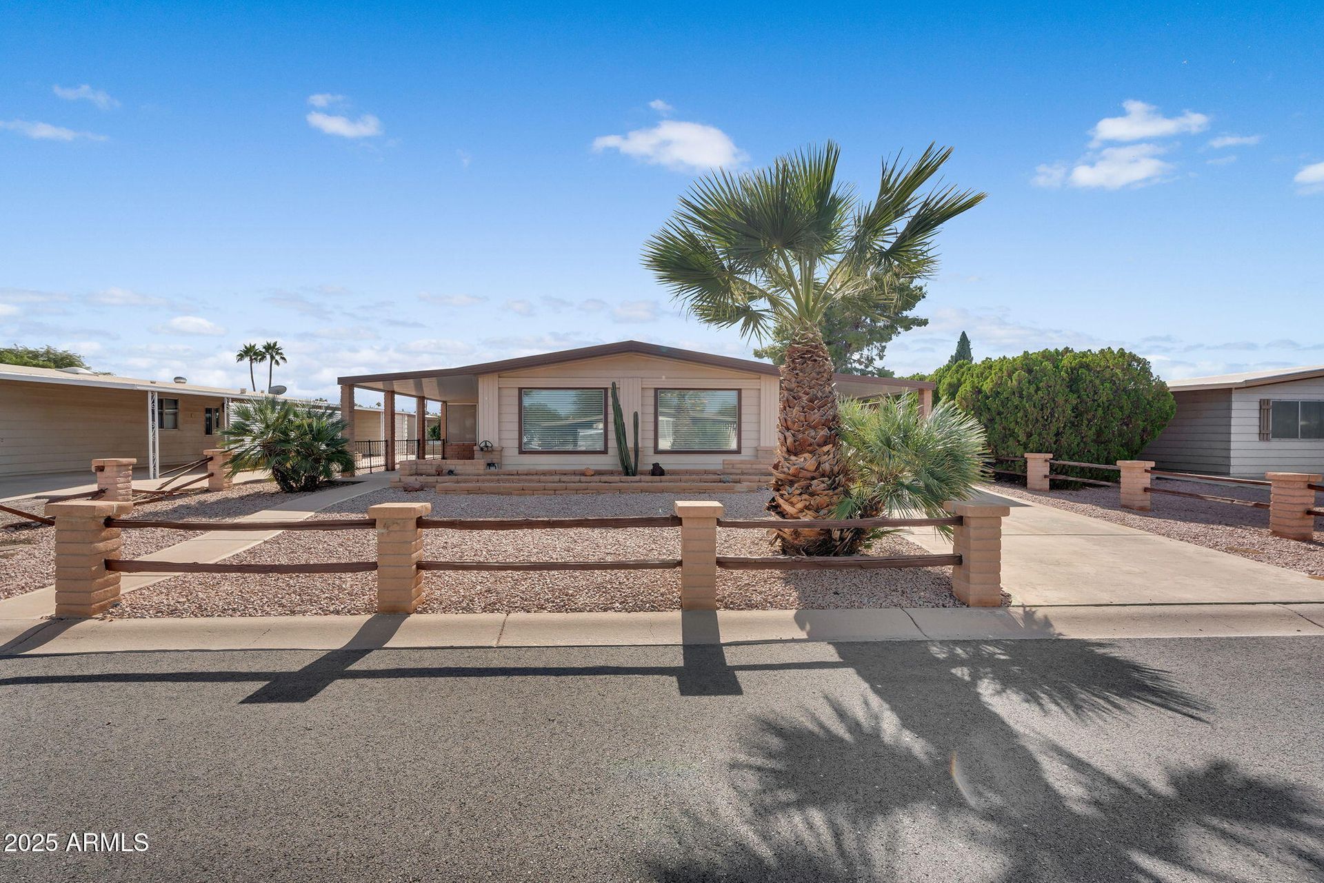 Single-story house with desert landscaping, a low brick wall, and a tall palm tree under a blue sky.