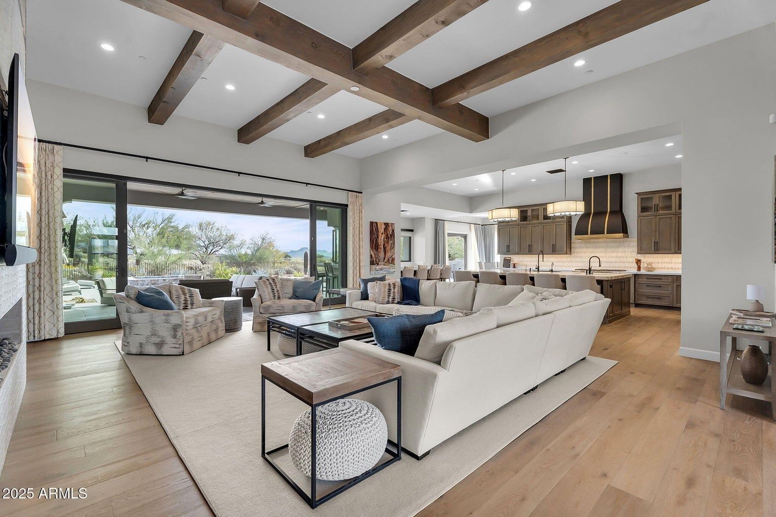 Bright open-plan living room with white sofa, exposed beams, fireplace, and large sliding doors to a patio