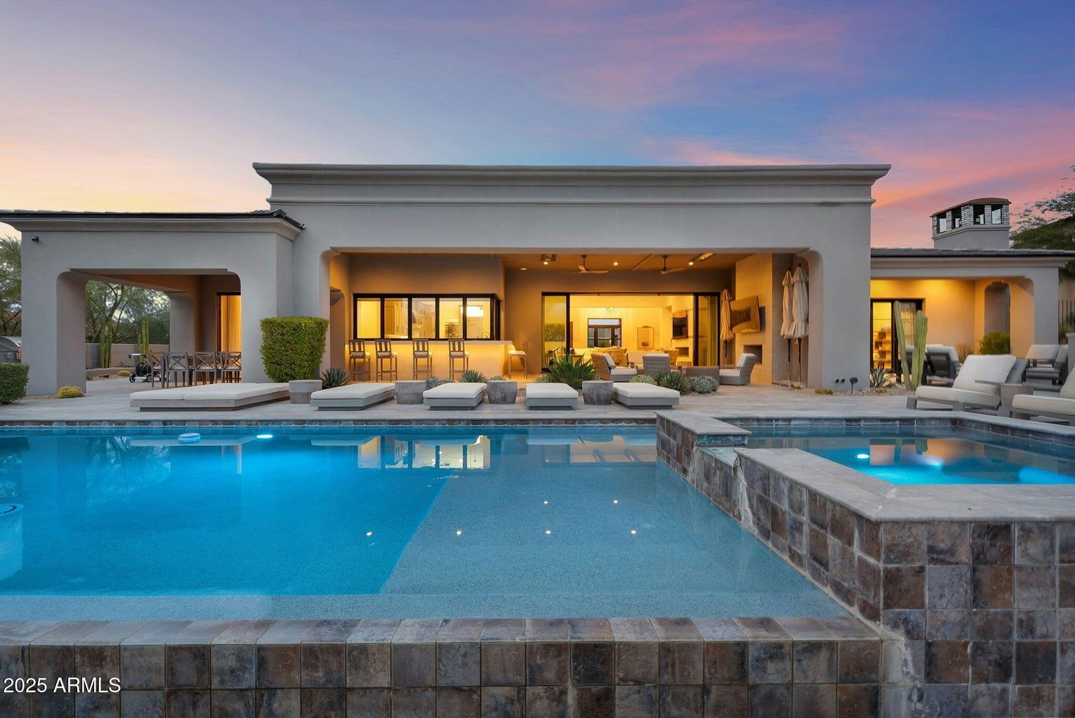 Luxury backyard patio with glowing pool and spa at sunset, with a modern house in the background