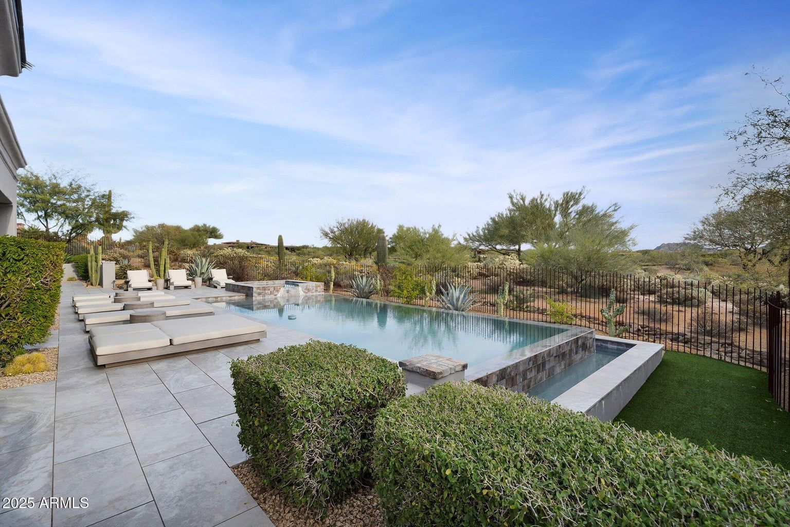 Modern backyard pool with lounge chairs, manicured hedges, and a patio under a bright blue sky