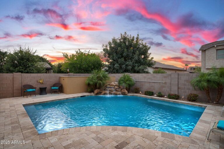 Backyard pool at sunset with pink clouds and patio seating