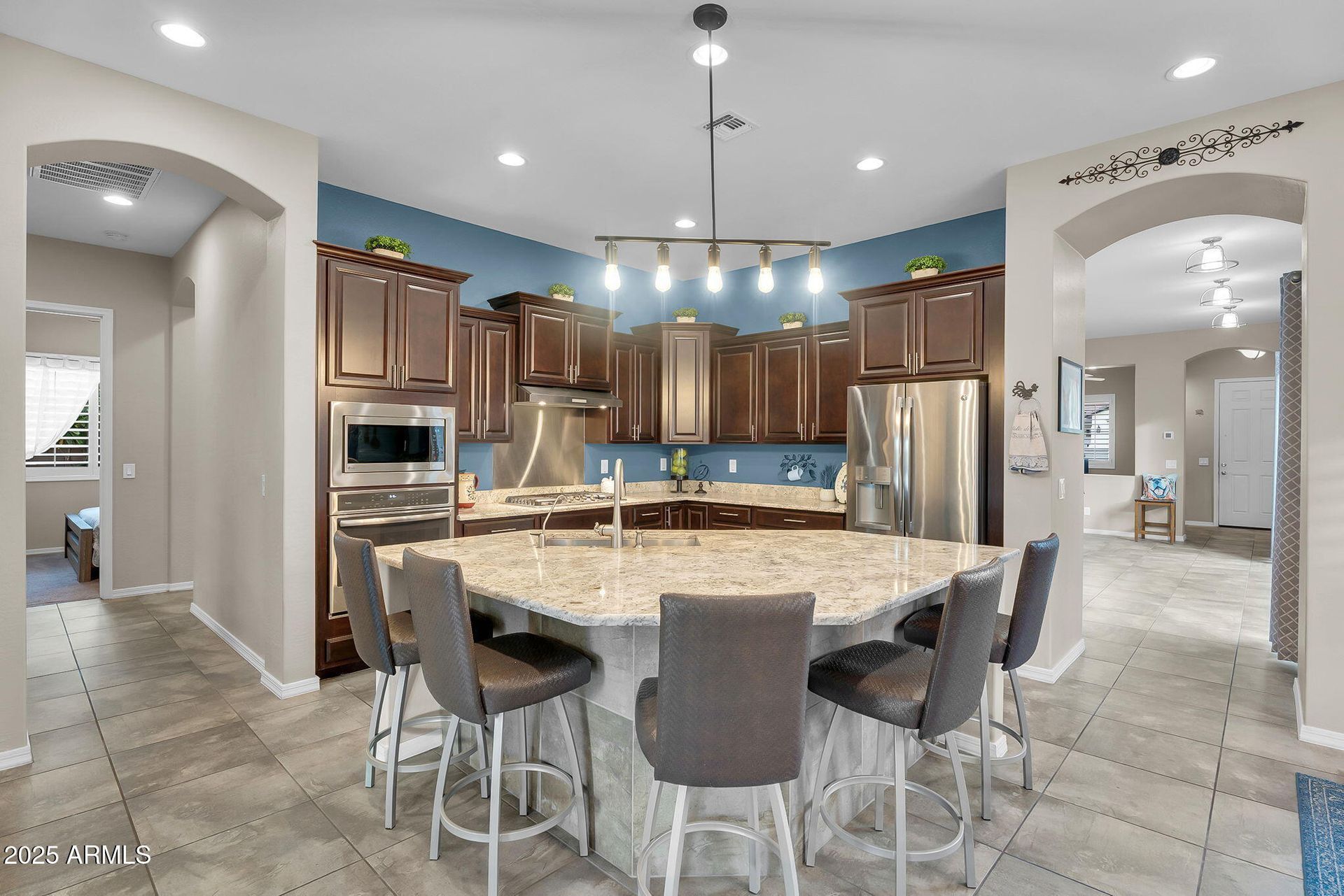 Spacious kitchen with granite island, dark wood cabinets, pendant lights, and tiled floor