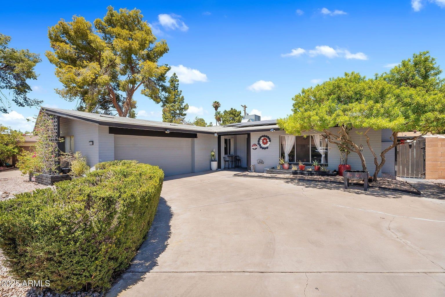 Single-story suburban house with a large driveway, garage, and desert landscaping under a blue sky
