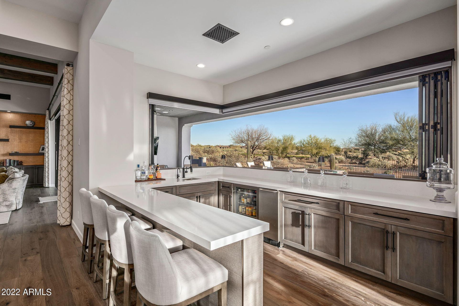 Modern kitchen with a marble island, bar stools, and large corner windows overlooking a scenic view