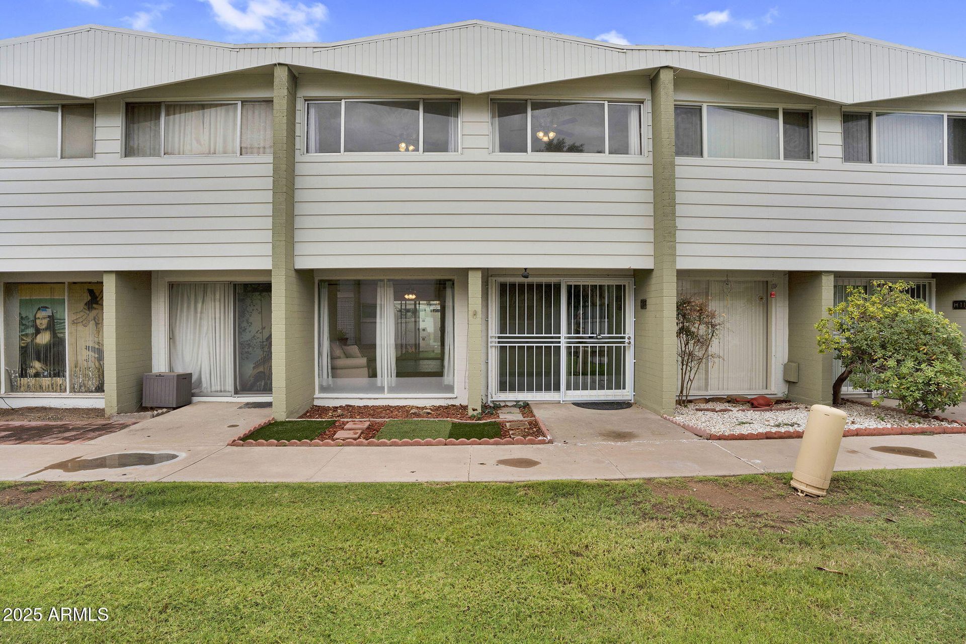 Row of beige townhouses with front doors, windows, and small lawns under a gray roofline
