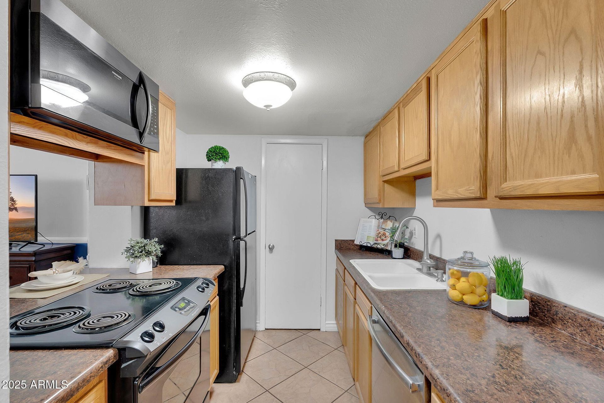 Narrow galley kitchen with wood cabinets, black refrigerator, white door, and tiled floor