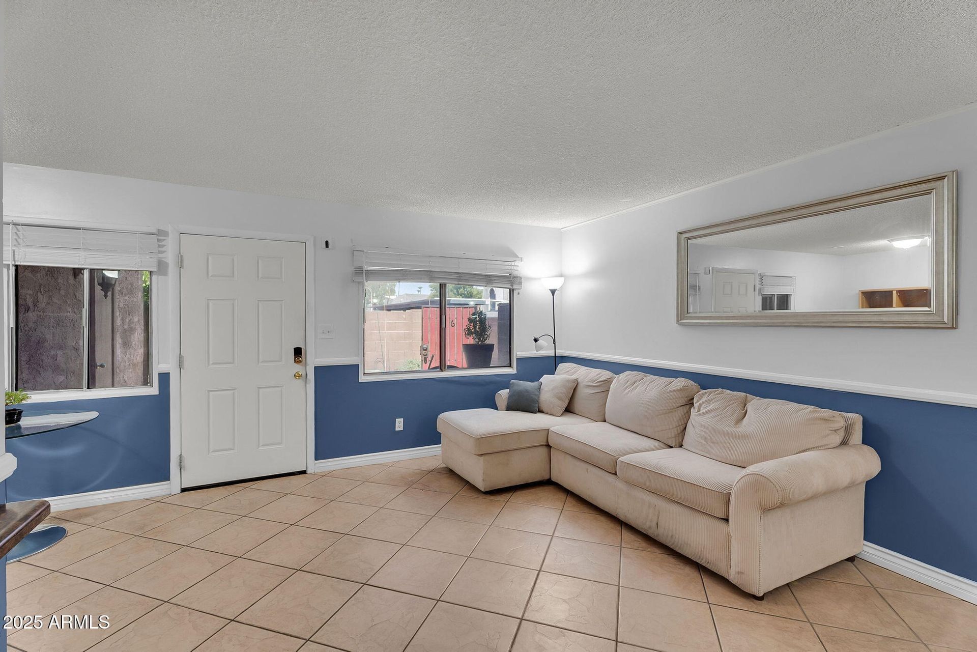 Bright living room with beige sectional, blue walls, tiled floor, and wall mirror