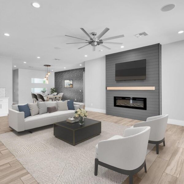 Bright modern living room with gray sofa, white chairs, fireplace, TV, and wood flooring