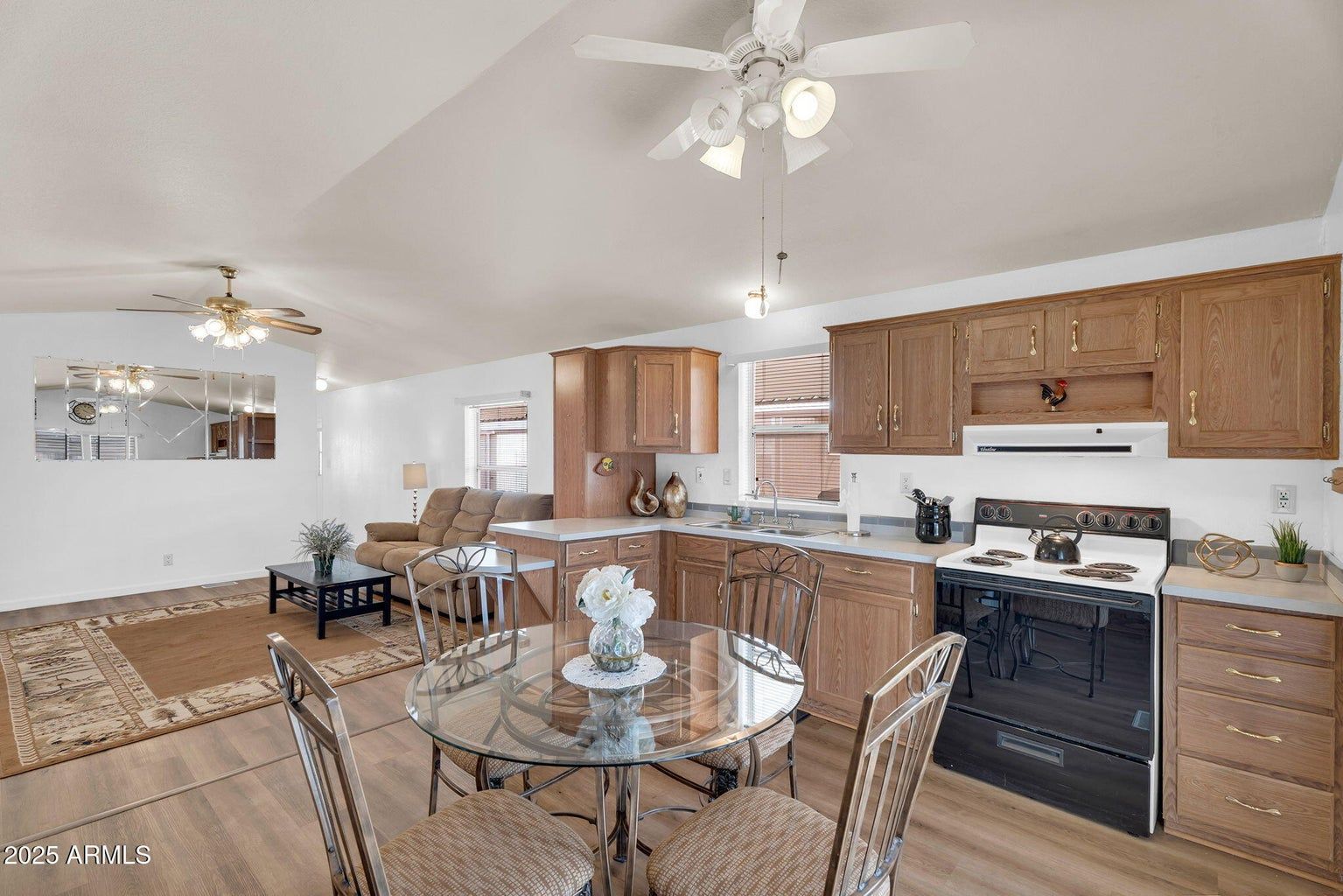 Bright kitchen with wood cabinets, black stove, glass dining table, and ceiling fans in an open layout.