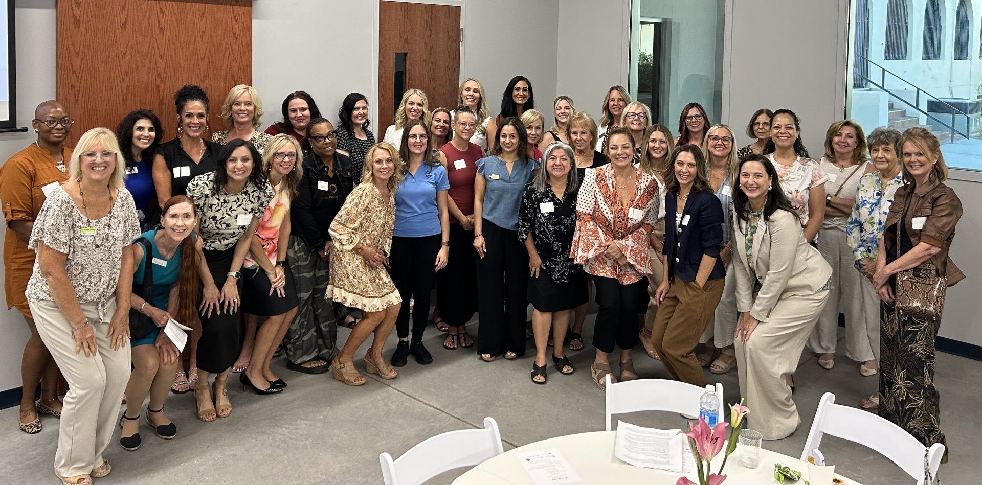 Group of people posing in a lobby, dressed in formal and semiformal attire, with tables in the foreground.
