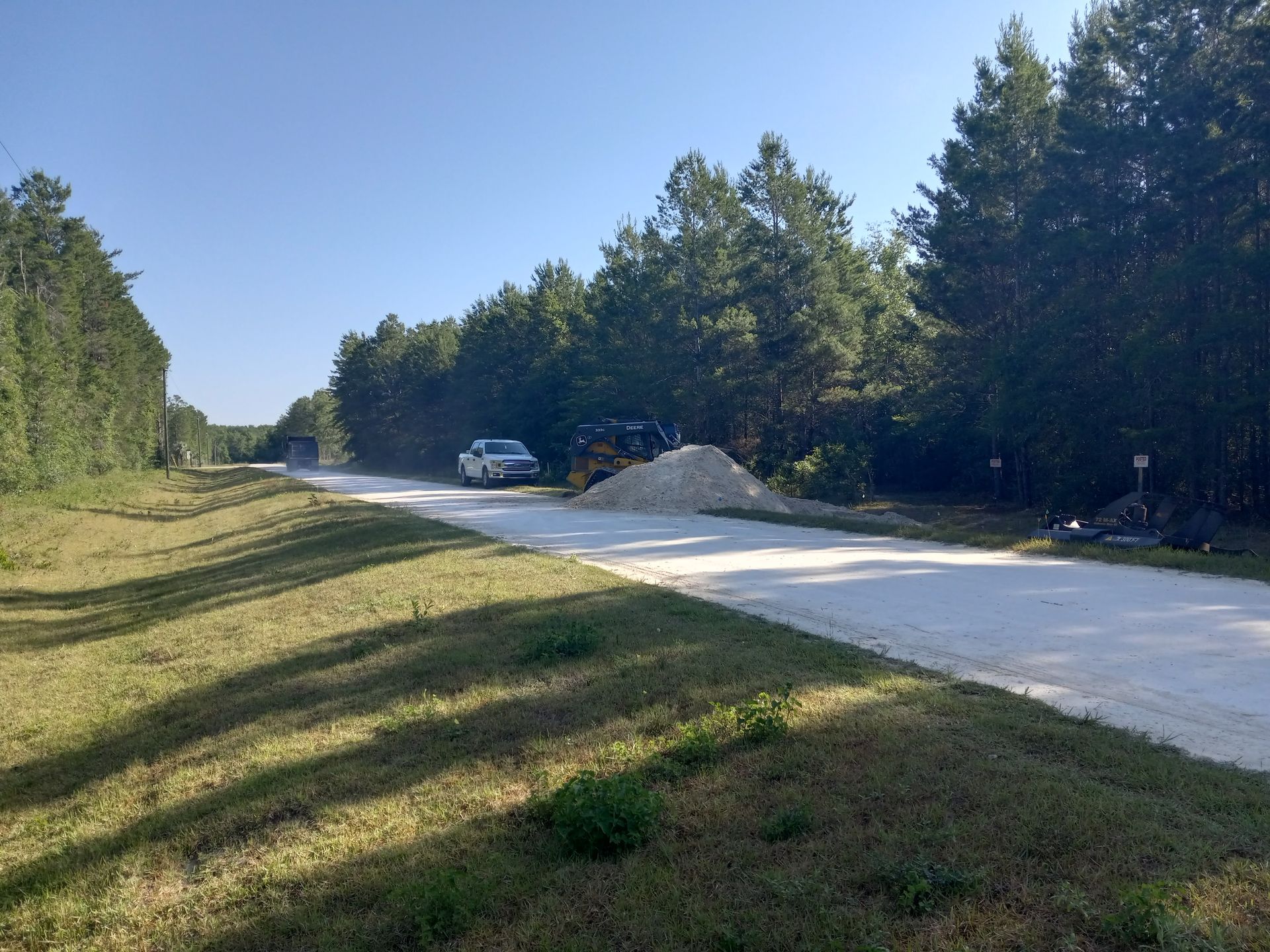 A gravel road with a white truck and a pile of gravel next to a forest.